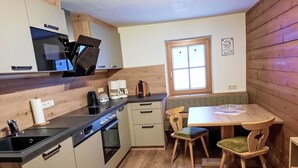 A compact kitchen with wooden cabinets, a built-in oven, a coffee maker, and a dining area with two chairs and a table. - Althaus 1 by Interhome (Neukirchen am Großvenediger)