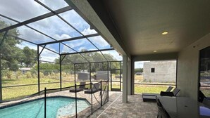 Un espace piscine extérieur abrité, doté d’une structure en verre, d’une terrasse en briques et de coins salon extérieurs.