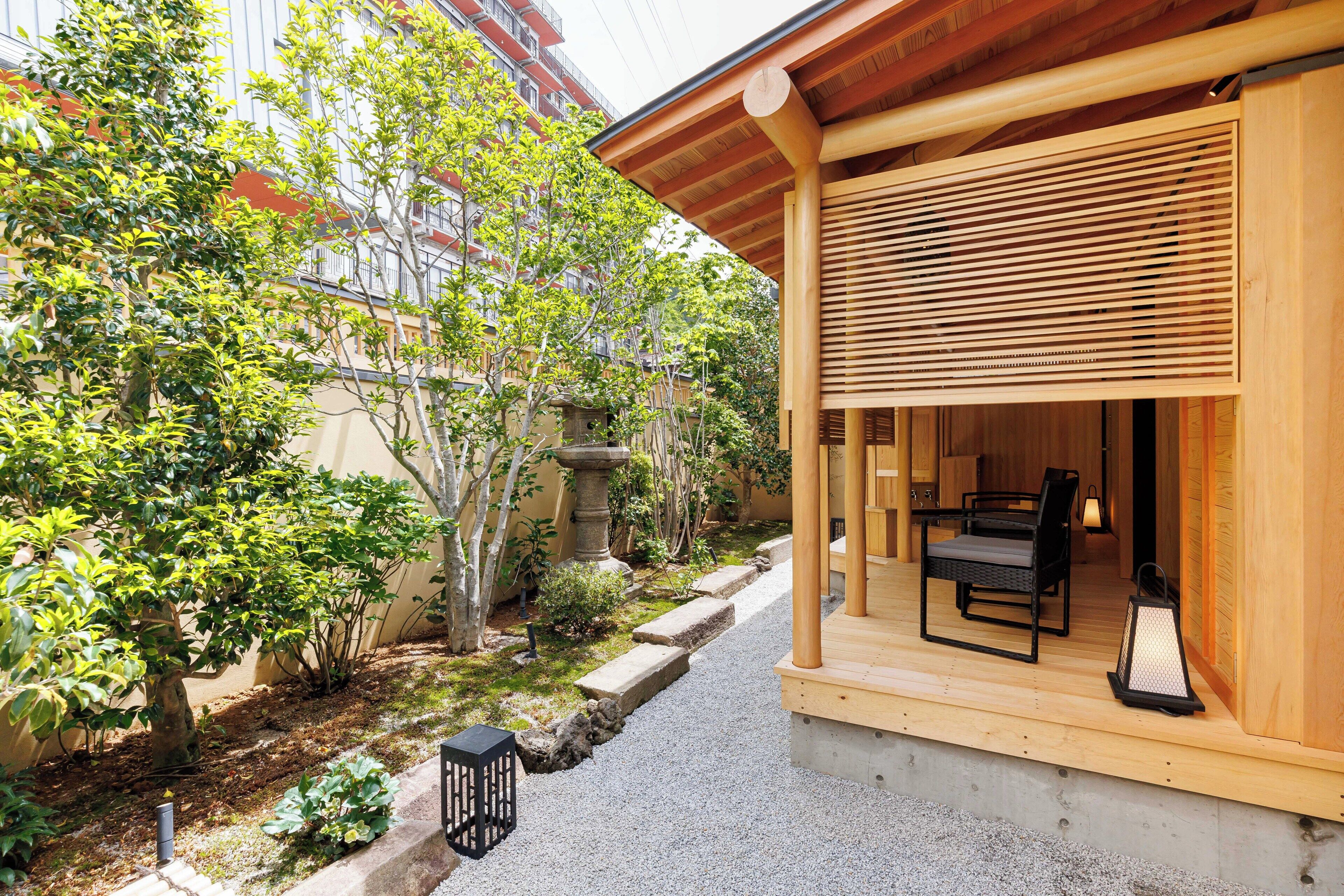 A wooden building with a covered porch, stone steps, and a garden with trees and plants.