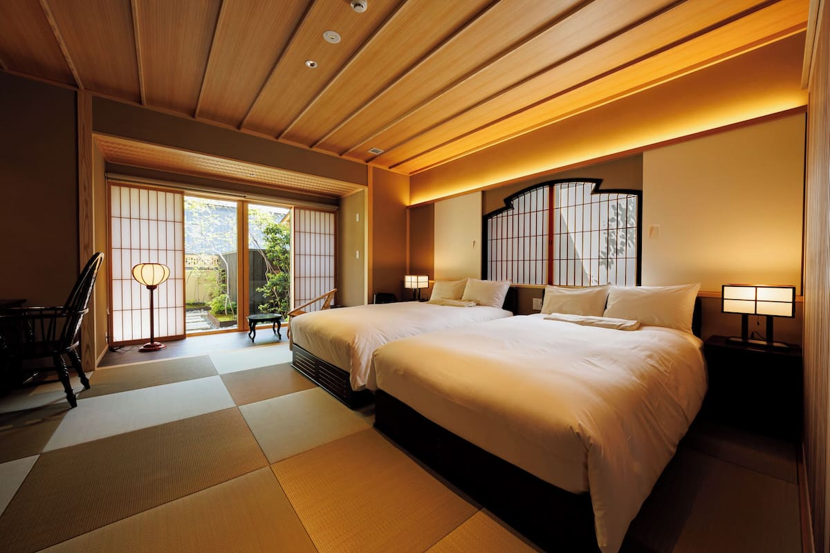 A traditional Japanese-style bedroom with tatami flooring, a large bed, sliding doors, and a view of the garden.