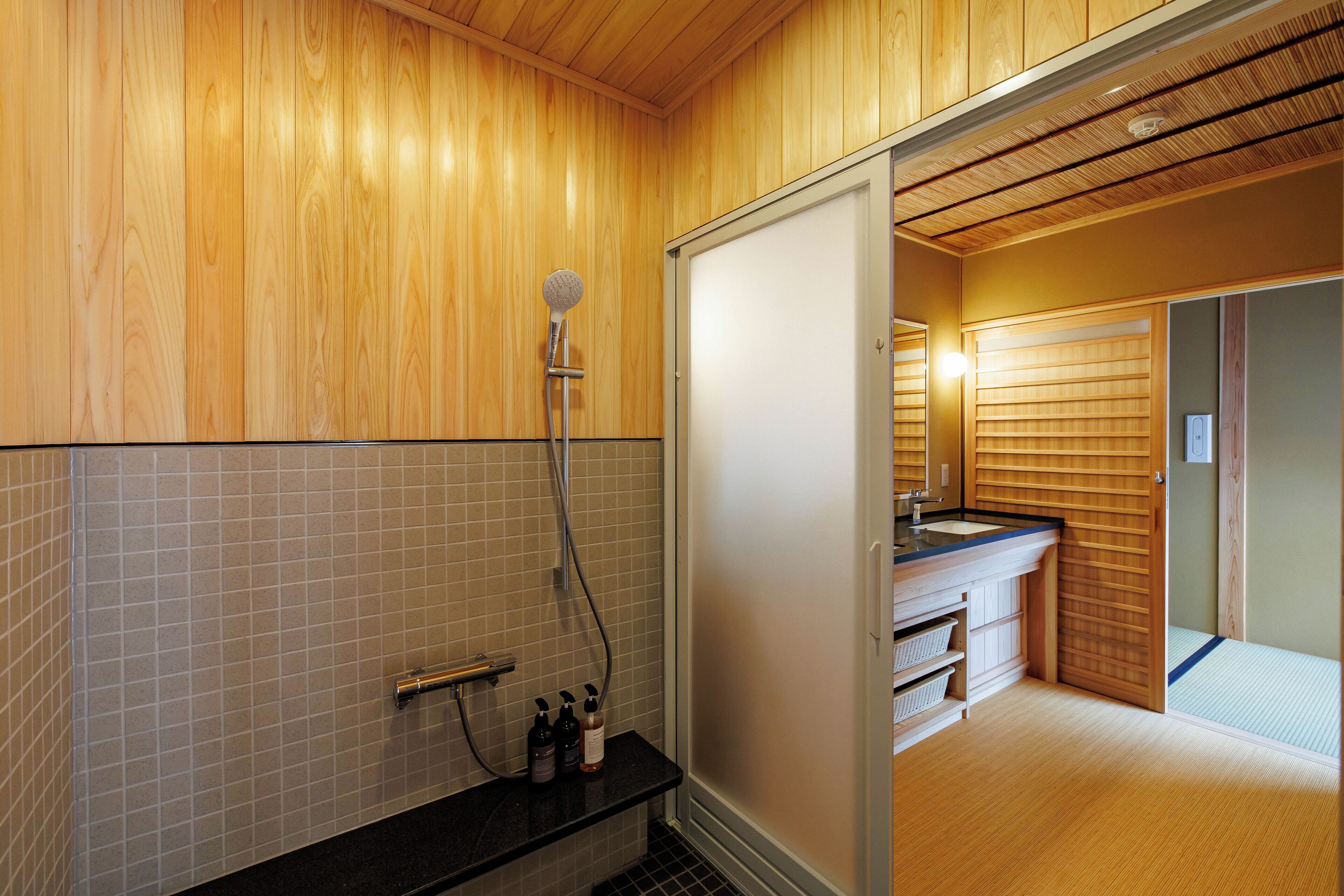 Une salle de bain moderne avec un lambris en bois, une douche équipée d’un pommeau de douche à main et un meuble-lavabo avec un évier et des rangements.