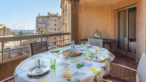Un balcón con mesa lista para comer, con vista a un puerto deportivo y edificios.