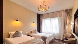 A hotel room with two beds, a chandelier, a large window with curtains, and a chair. - Amar Hotel Ulaanbaatar live  (Ulaanbaatar)