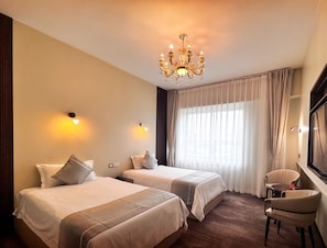 A hotel room with two beds, a chandelier, a large window with curtains, and a chair. - Amar Hotel Ulaanbaatar live  (Ulaanbaatar)