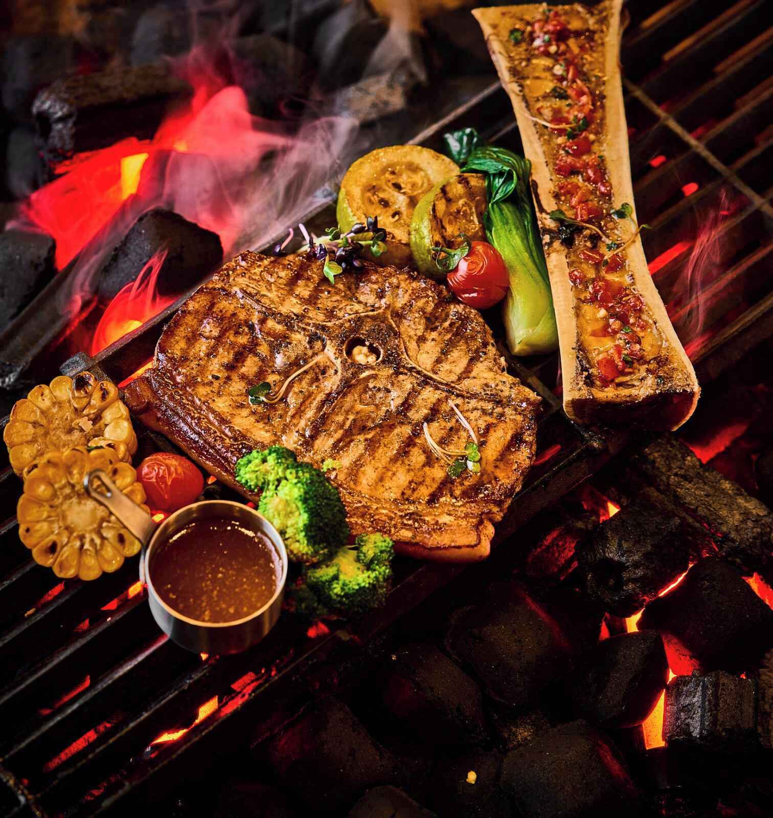 A grill with various meats and vegetables, including a steak, broccoli, and a whole fish.