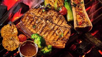 A grill with various meats and vegetables, including a steak, broccoli, and a whole fish.