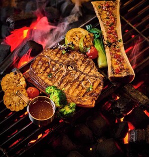 Un plat grillé composé de différentes sortes de viande et de légumes, notamment un steak, des brocolis et un poisson entier.