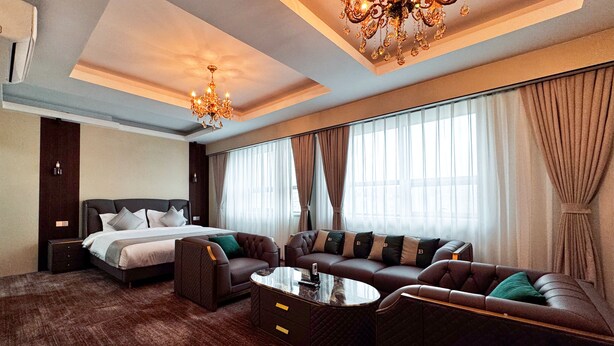 Ein geräumiges Hotelzimmer mit einem großen Bett, einer Ledersitzgruppe, einem Couchtisch und einem Kronleuchter.