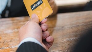A person holding a yellow card with a logo, seated at a wooden table. - Amar Hotel Ulaanbaatar live  (Ulaanbaatar)