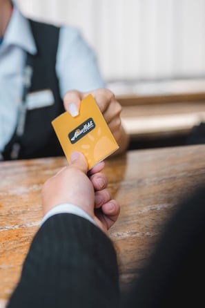 A person holding a yellow card with a logo, seated at a wooden table. - Amar Hotel Ulaanbaatar live  (Ulaanbaatar)