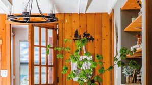 Ambiente interno in legno con tavolo da pranzo, sedie, lampadario e una porta che dà sull'esterno.
