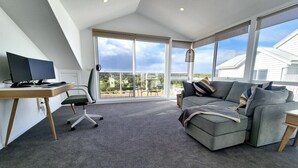 Un salon moderne avec une grande fenêtre, un canapé gris, un bureau avec un ordinateur et un fauteuil.