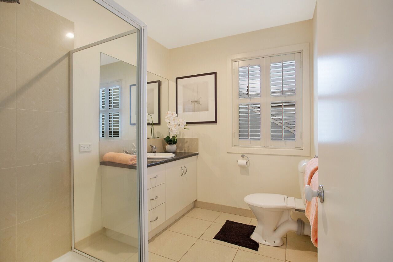 Een moderne badkamer met een douchecabine van glas, een wit toilet en een wastafel met aanrechtblad.