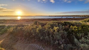 Un paysage côtier avec un coucher de soleil, une plage de sable et une jetée qui s’avance dans l’eau.