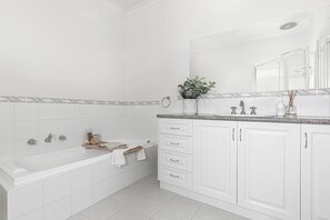 A modern bathroom with a white bathtub, a sink with a mirror, and a cabinet with drawers. - `Beach Side` Warrnambool CBD (Warrnambool)