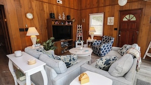 A cozy living room with a grey sofa set, a flat-screen TV, a white coffee table, and a small white table with a lamp. - Shore 'Nuf - 3 BR Oceanside in Duck (Duck)