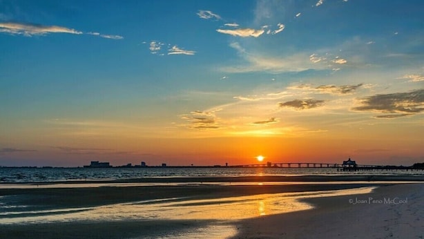 Een zonsondergang boven een strand met een pier die het water in reikt.