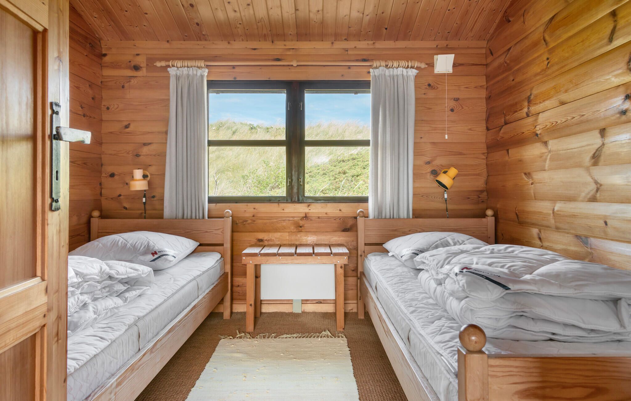 Une cabane avec deux lits en bois, un banc et une fenêtre avec des rideaux.