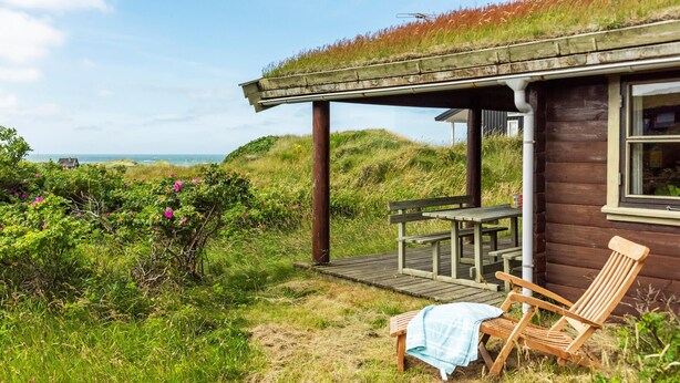 A wooden cabin with a thatched roof, a wooden deck, and a bench. - 2 bedroom lovely home in Saltum (Saltum)