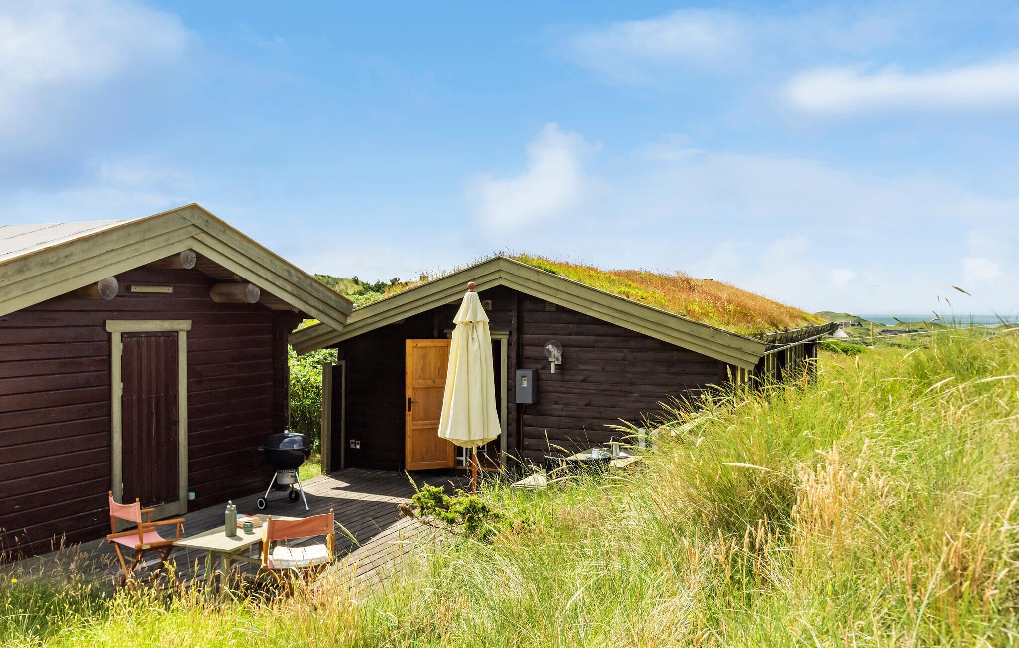 Two wooden cabins with green roofs, a barbecue, and outdoor seating.