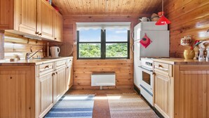 A compact kitchen with wooden cabinets, a window with a view, a stove, and a refrigerator. - 2 bedroom lovely home in Saltum (Saltum)