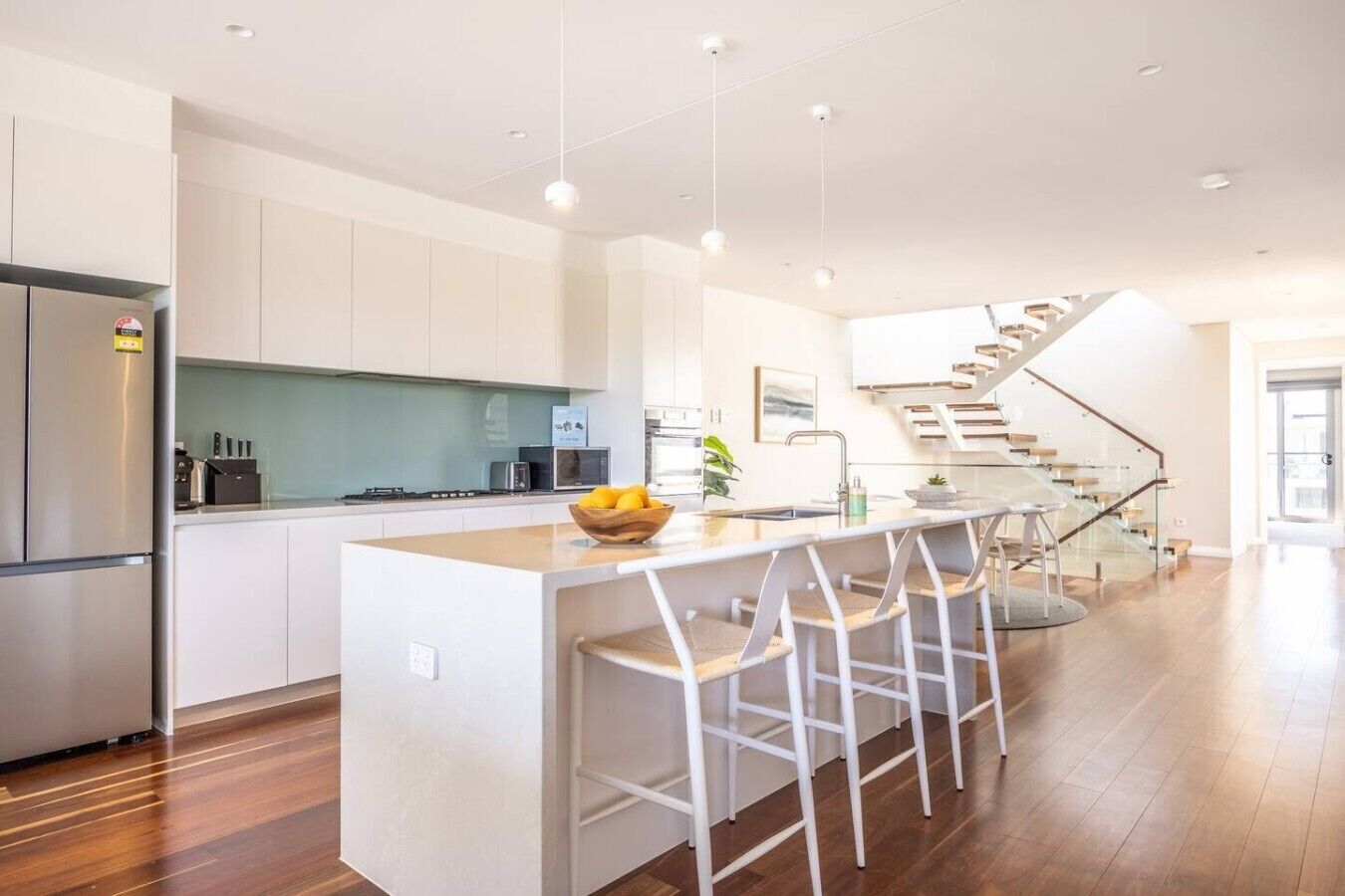 A modern kitchen with a central island, bar stools, a refrigerator, and a staircase leading to another level.