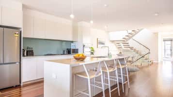 A modern kitchen with a central island, bar stools, a refrigerator, and a staircase leading to another level.