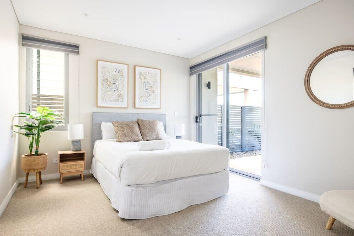 A bedroom with a bed, bedside tables, a potted plant, and a sliding glass door leading to a balcony.