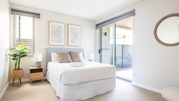 A bedroom with a bed, bedside tables, a potted plant, and a sliding glass door leading to a balcony.