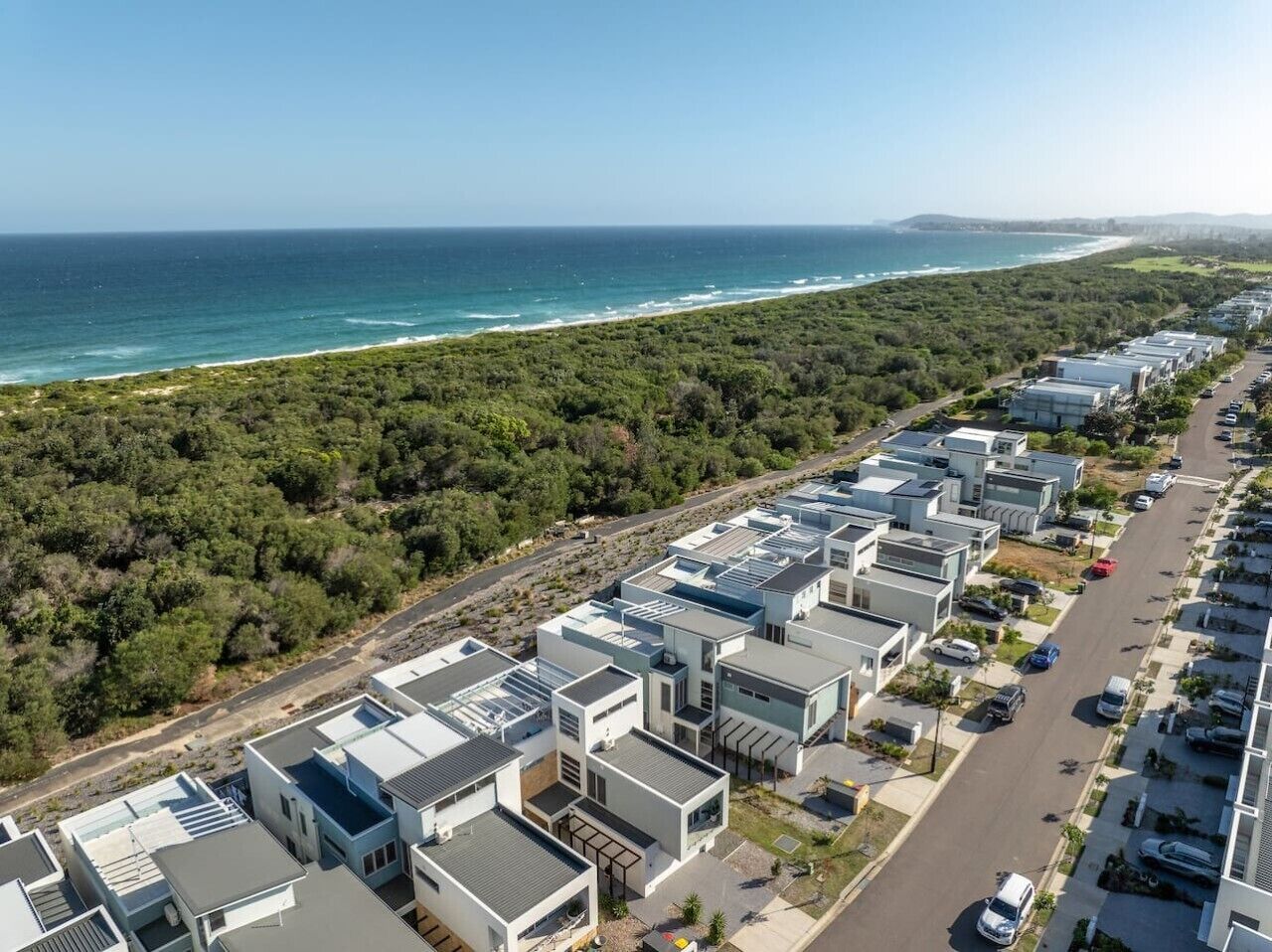 A coastal residential area with modern buildings, a road, and a beach.