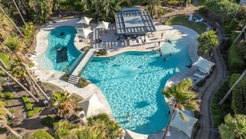 An aerial view of a resort with a large, curved swimming pool surrounded by palm trees and lounge chairs.