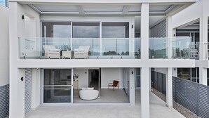 A modern two-story house with a balcony, sliding glass doors, and a small outdoor seating area. - Oceanfront Oasis | Stylish 4BR w/ Epic Terrace (Magenta)