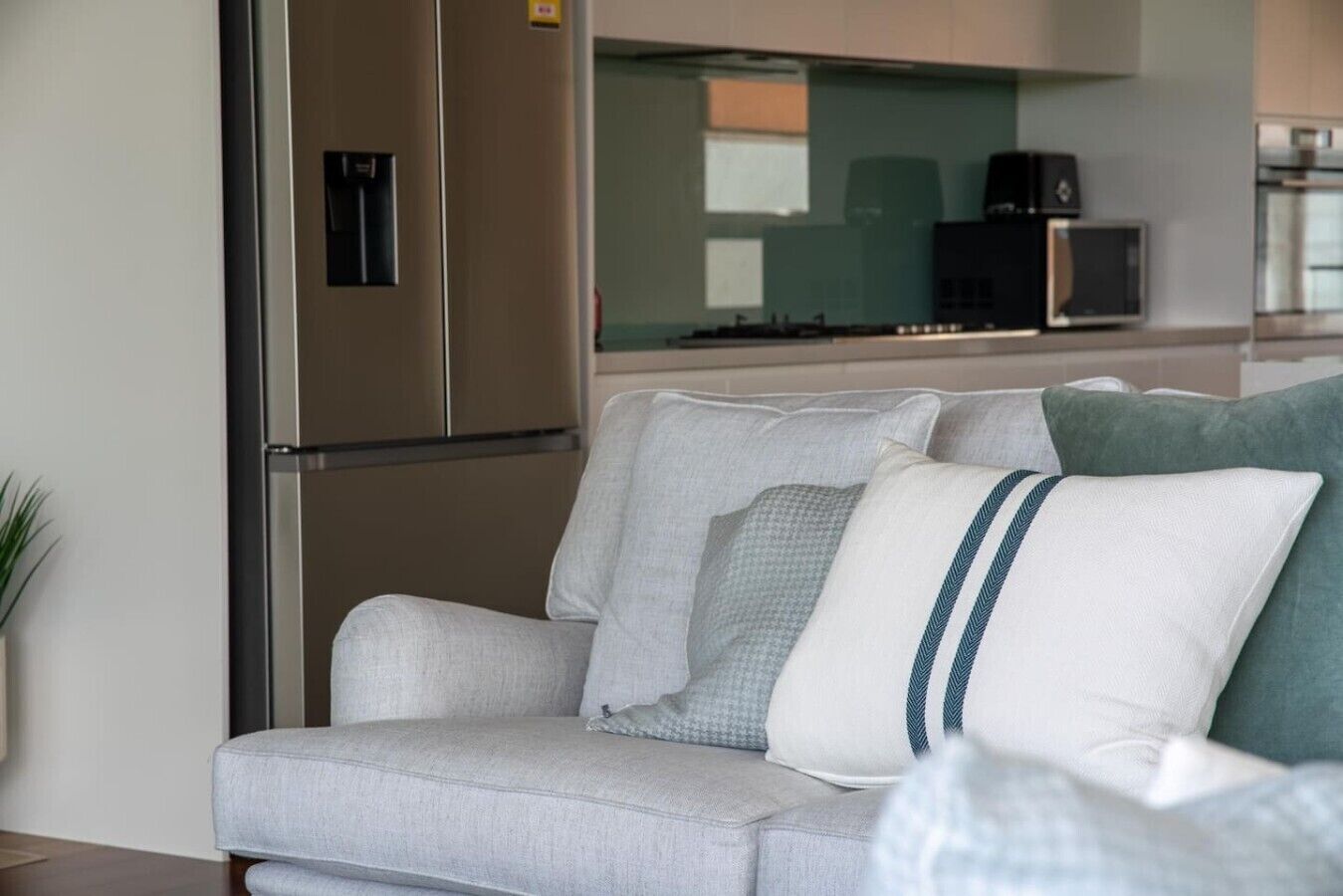 A modern kitchen with stainless steel appliances, a grey sofa with patterned cushions, and a view of the living area.