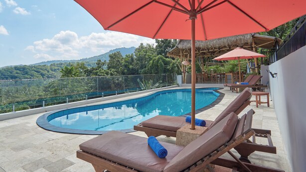 A poolside area with lounge chairs and umbrellas, overlooking a natural landscape. - Attara Hills Sunset Villa Senggigi (Senggigi)