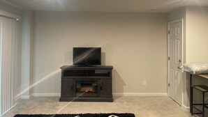 A living room with a fireplace, a television on a wooden entertainment unit, and a door to the right. - Stylish Decor Studio (Tega Cay)