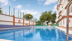 En swimmingpool med flisekant, omgivet af et hegn og redningskranse.