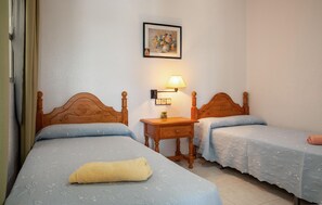 Two single beds with wooden headboards and floral-patterned bedspreads, a nightstand with a lamp, and a framed picture adorn this cozy space.