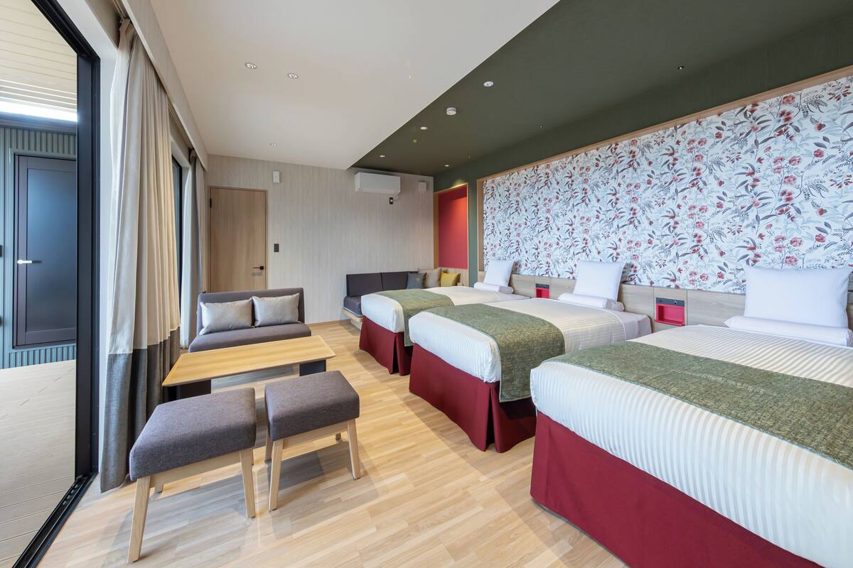 Une chambre d’hôtel moderne avec un grand lit, deux petits lits, un canapé et un banc.