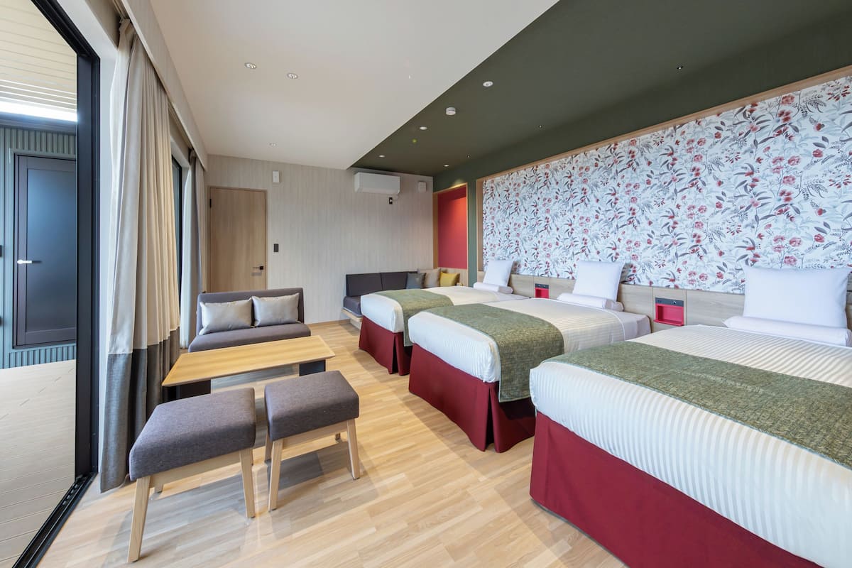 A modern hotel room with a large bed, two smaller beds, a sofa, and a bench.