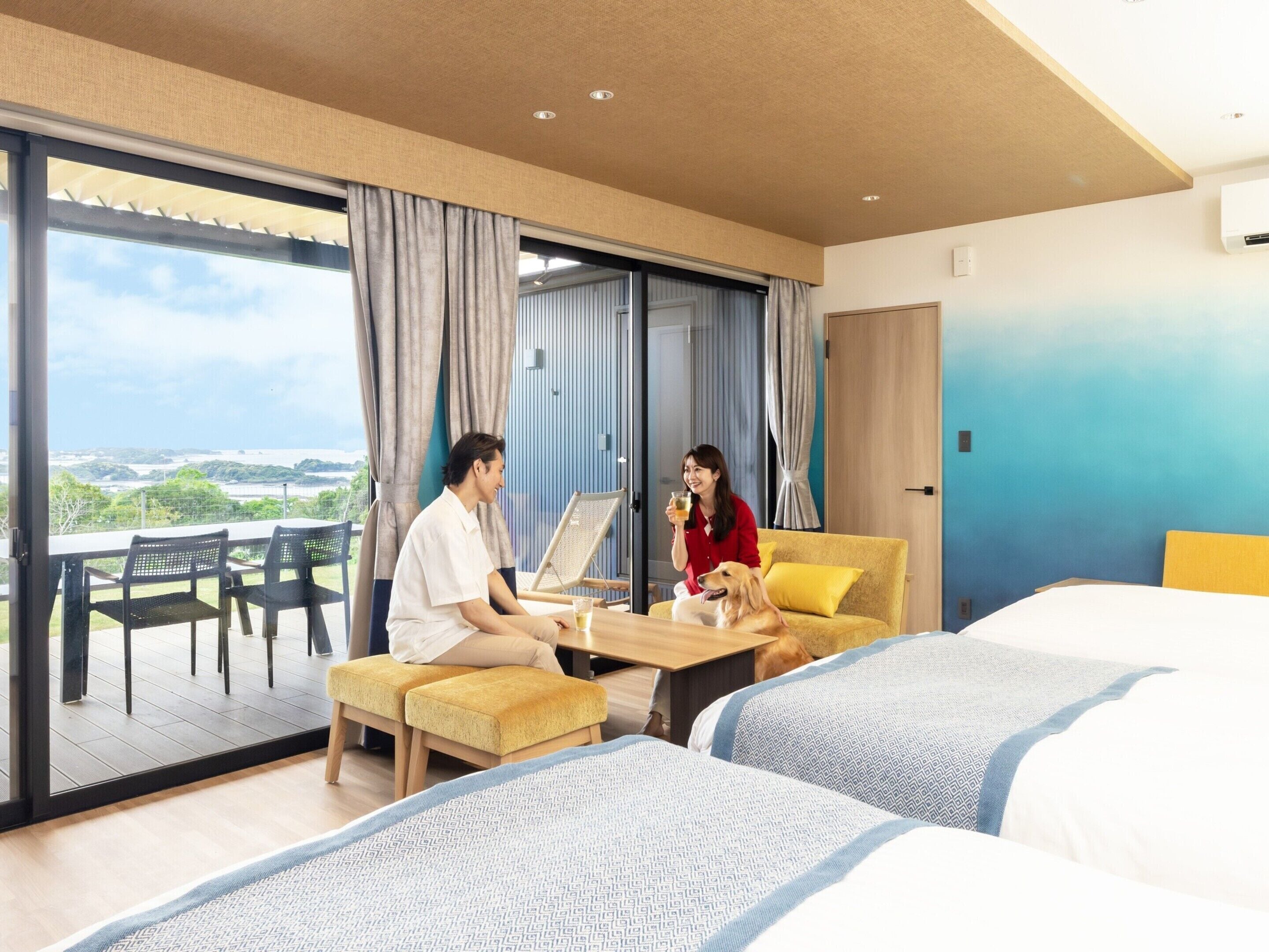 A hotel room with a balcony, a sofa, a table, and two beds.