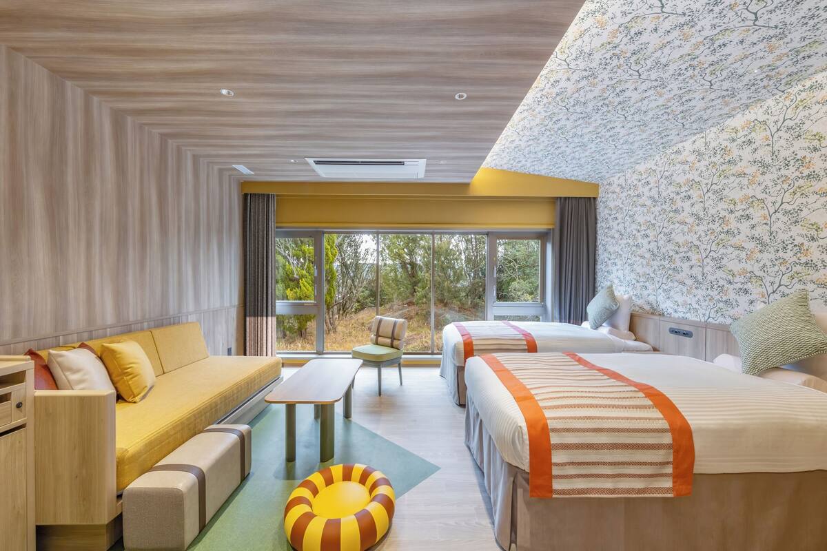 Une chambre d’hôtel moderne avec un canapé, deux lits, une petite table et une vue sur l’extérieur.