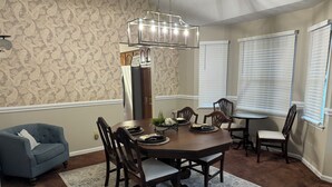 A dining room with a wooden table, chairs, a chandelier, and a blue armchair. - Welborn House - Creekside  (Mountain City)