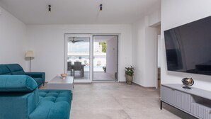 Ein modernes Wohnzimmer mit türkisfarbenen Sofas, einem Flachbildfernseher und einer Glastür, die zu einem Essbereich im Freien führt.