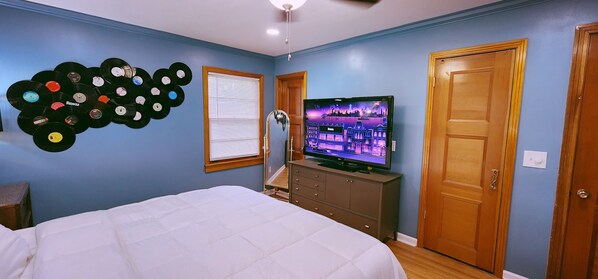 Une chambre à coucher avec un lit, une commode, un téléviseur et un mur décoré de disques vinyle.