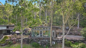 A modern house with a glass facade, surrounded by a stone wall and dense forest. - Saltwater Creek - immerse yourself in nature (Barringella)