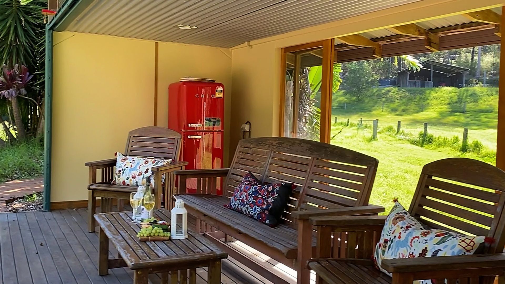 A covered outdoor seating area with wooden furniture and a red refrigerator.
