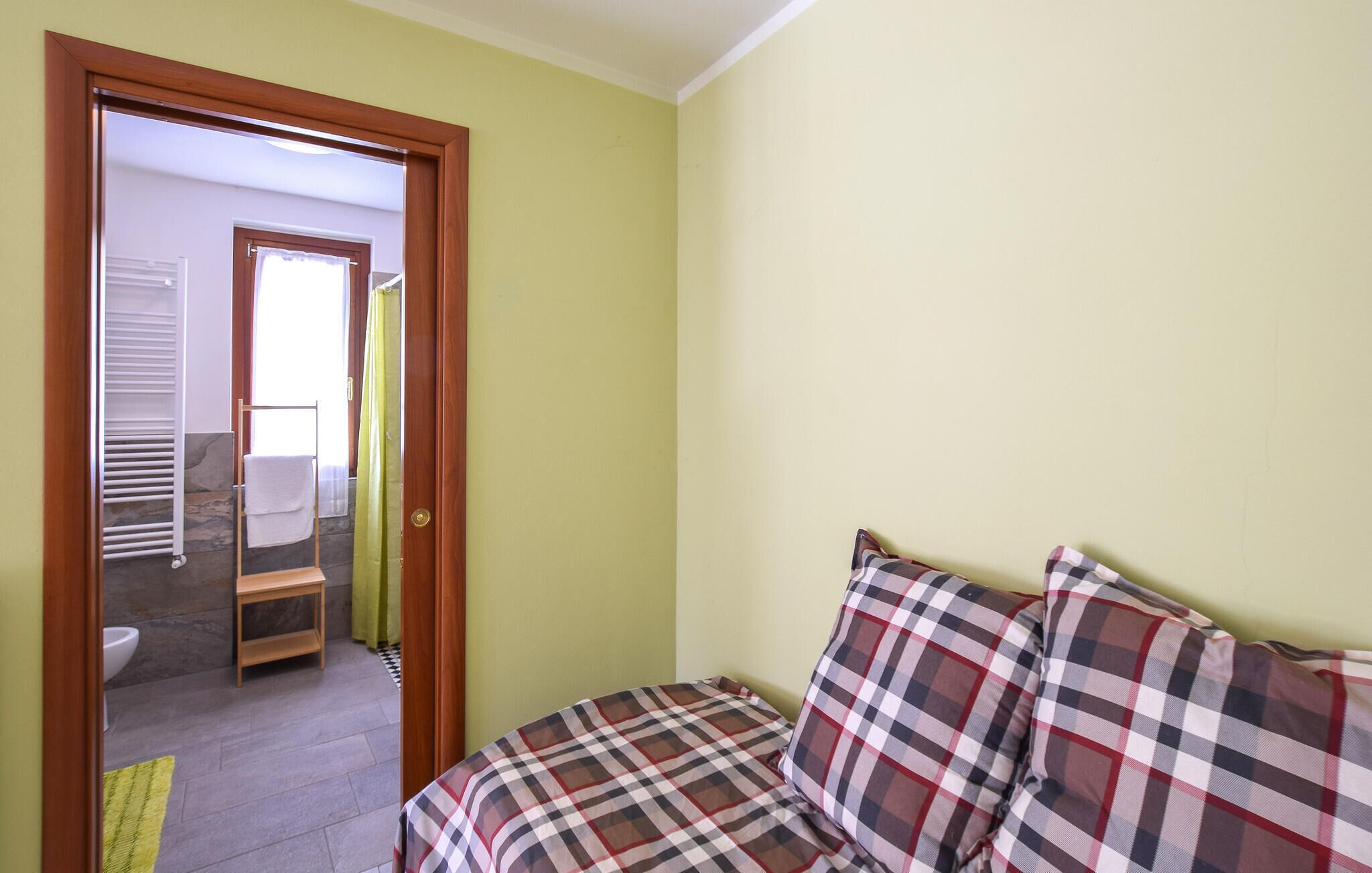 Une chambre à coucher avec un lit, une porte donnant sur une salle de bain, et une vue sur la salle de bain, où l’on aperçoit un porte-serviettes et des toilettes.