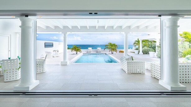 Un espace piscine avec vue sur l’océan, des colonnes blanches et des sièges d’extérieur.