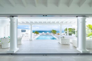 A pool area with a view of the ocean, white columns, and outdoor seating. - La Perla Bianca - 1 BR Beachfront Luxury Villa Offering Utmost Privacy (Les Terres Basses)