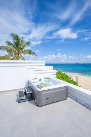 Uma banheira de hidromassagem numa varanda com vista para a praia e o oceano.